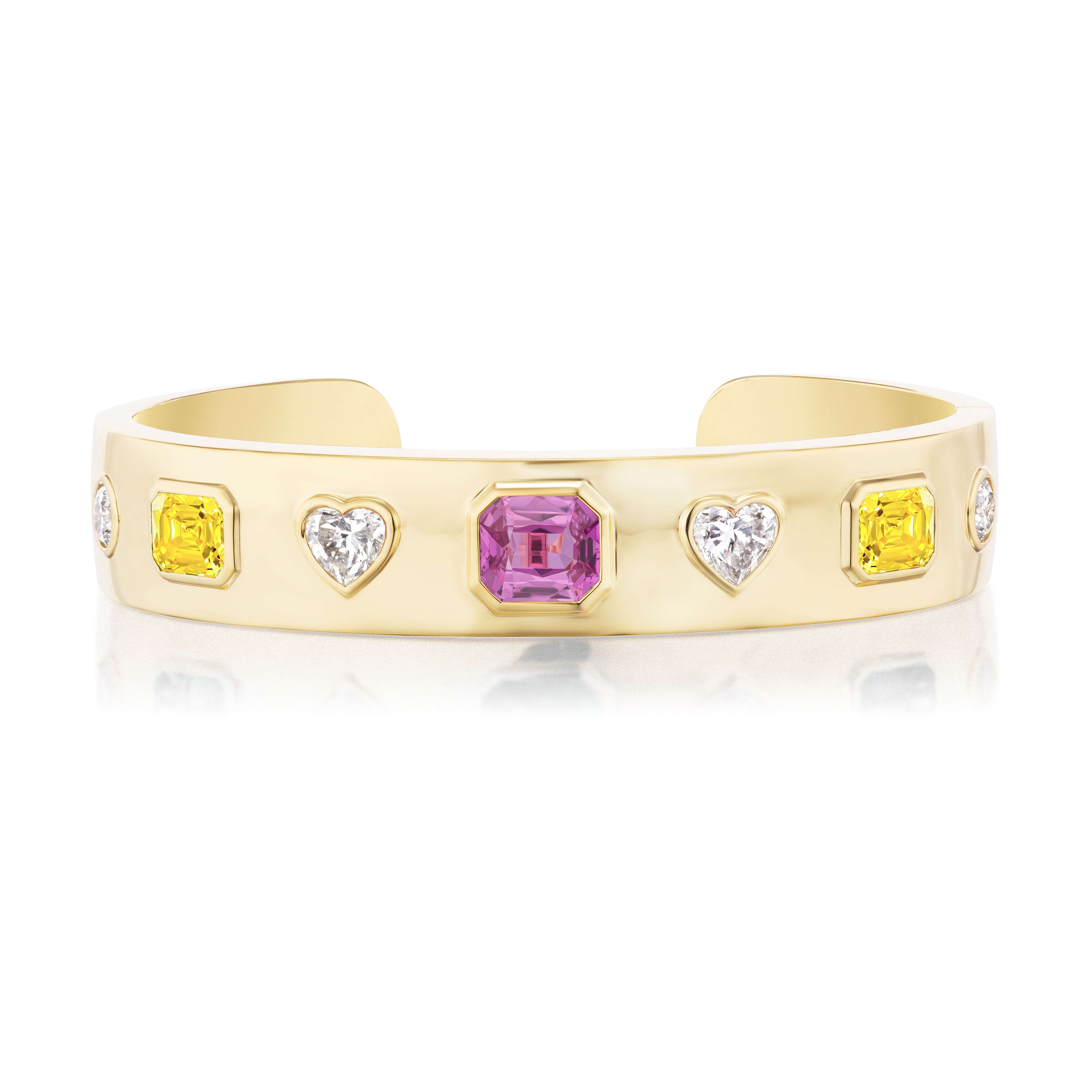 The Bezel Set Mixed Shape White, Yellow Diamond, and Sapphire Bangle features a central pink sapphire with heart-shaped white stones and yellow diamonds set symmetrically in 18K yellow gold.
