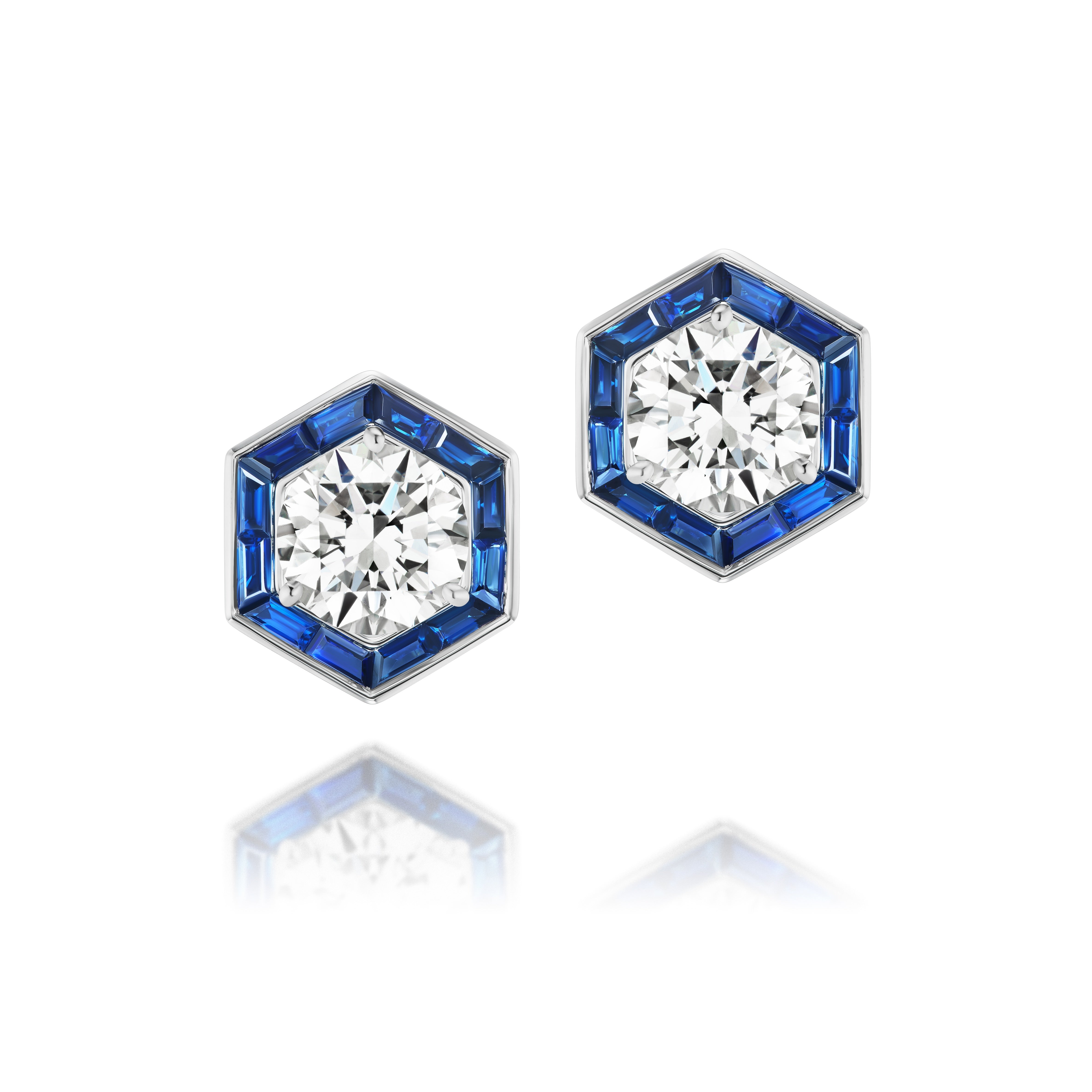 Hexagonal Trapezoid Sapphire Stud Ear Jackets with a central round diamond, blue sapphires, and silver setting. Shown on a white background with subtle reflection, these bespoke ear jackets exude modern elegance.