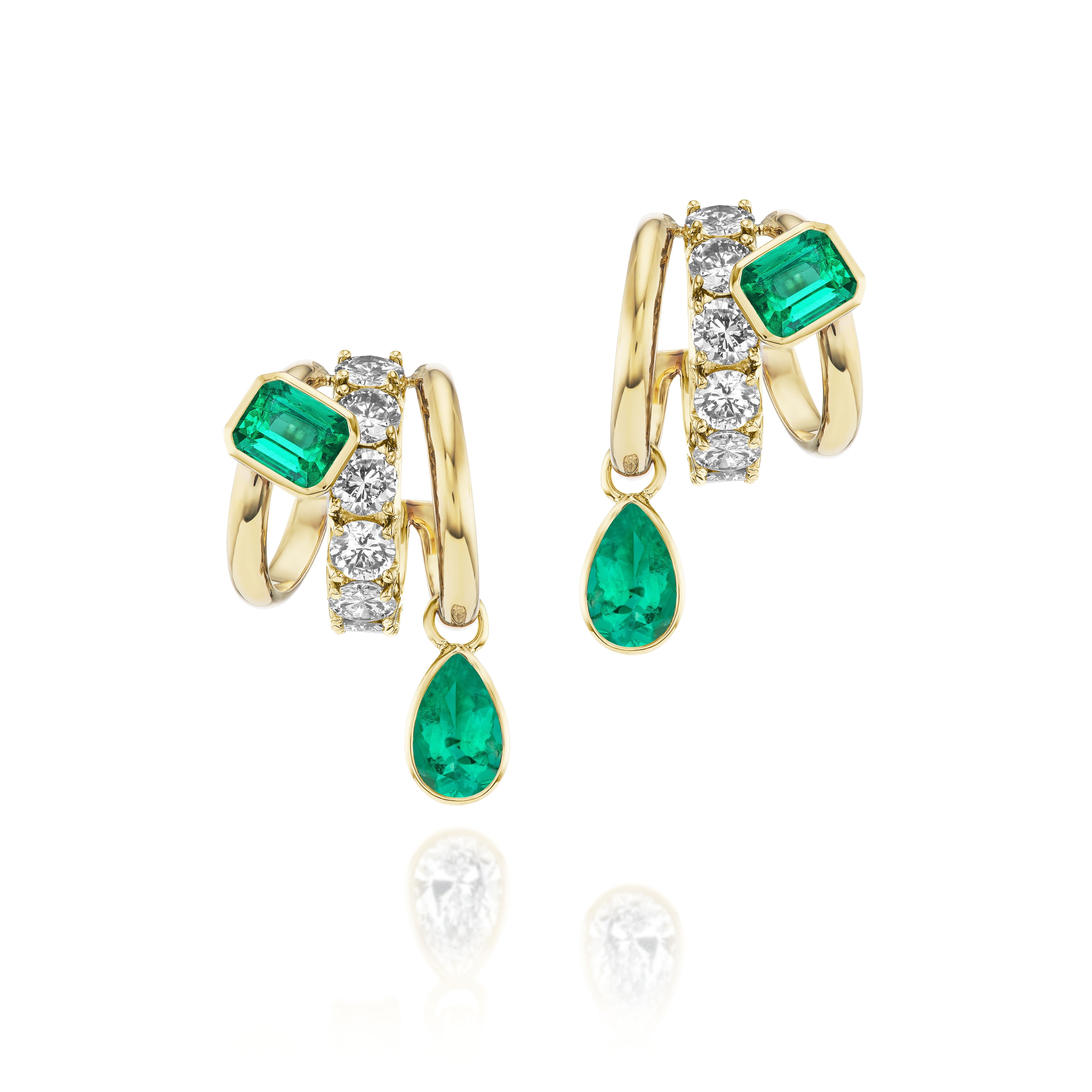 Huggie Earrings in Yellow Gold featuring round diamonds, one emerald cut and one pear shape emerald, set in 18K yellow gold and displayed on a white background.
