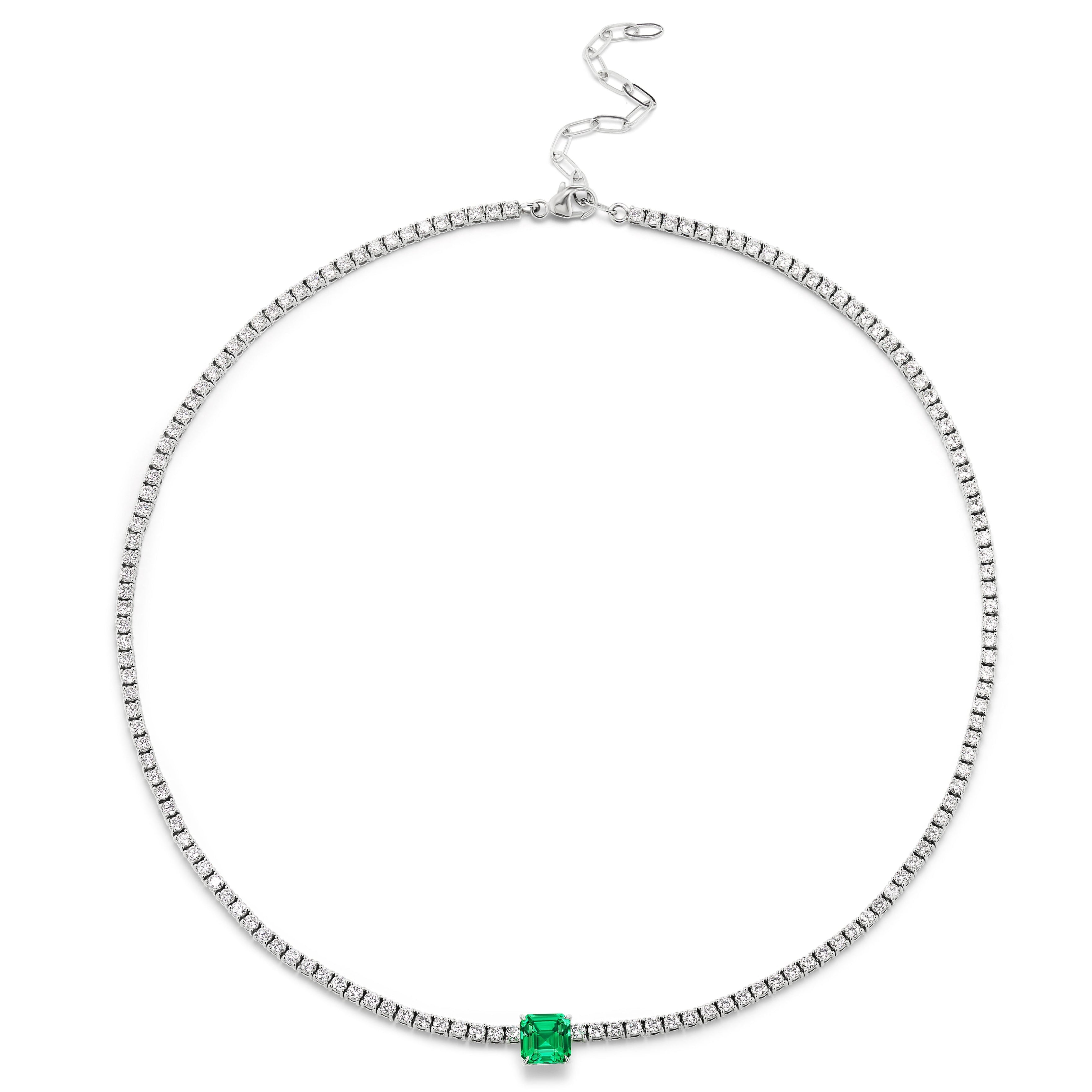 The Classic Tennis Necklace features an Asscher cut emerald centerpiece set in 18k white gold with small clear stones, displayed flat on a white background.