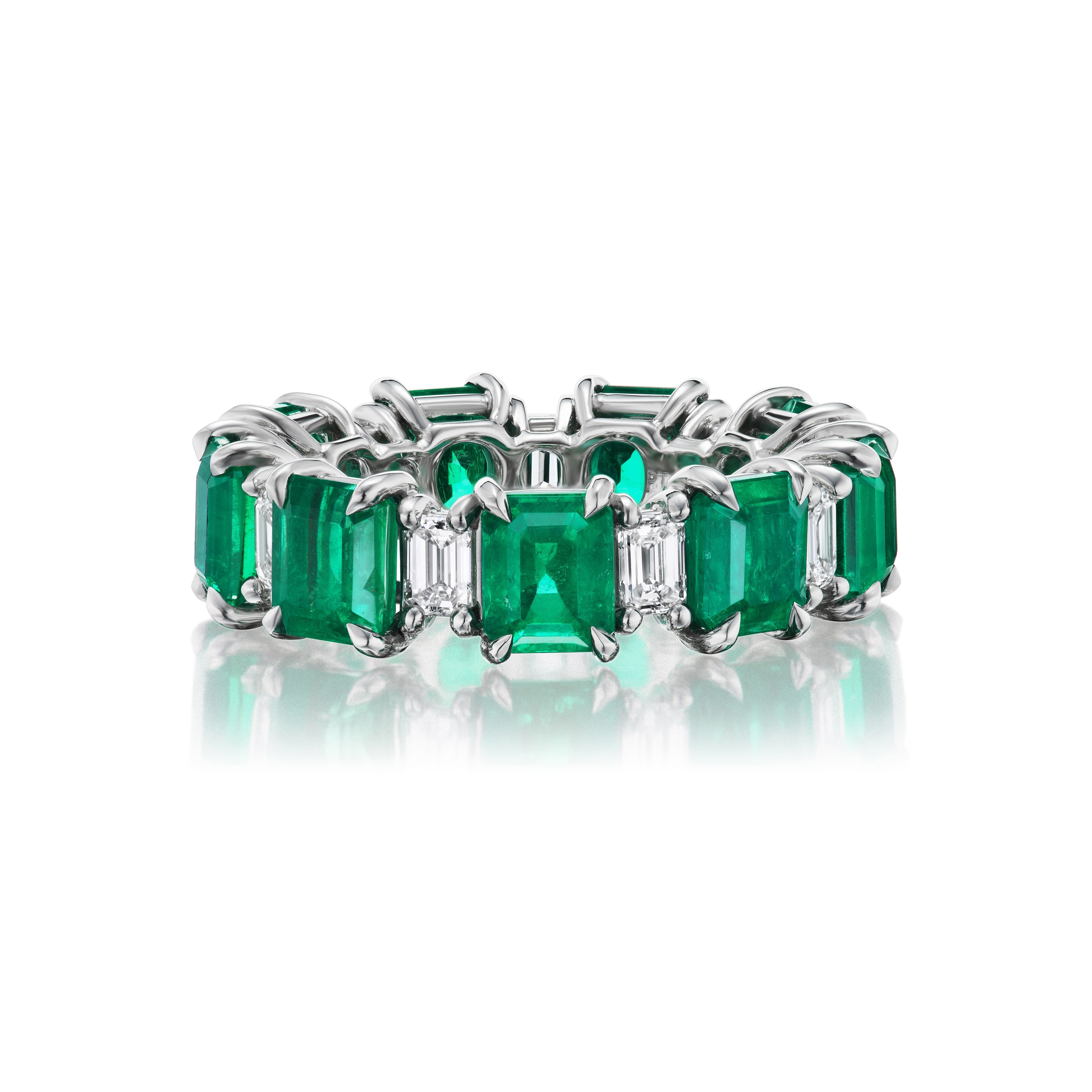 The Alternating Emerald Cut Diamond and Emerald Eternity Band is a platinum ring with rectangular emeralds and emerald cut diamonds in a continuous band, reflecting light on a white background.