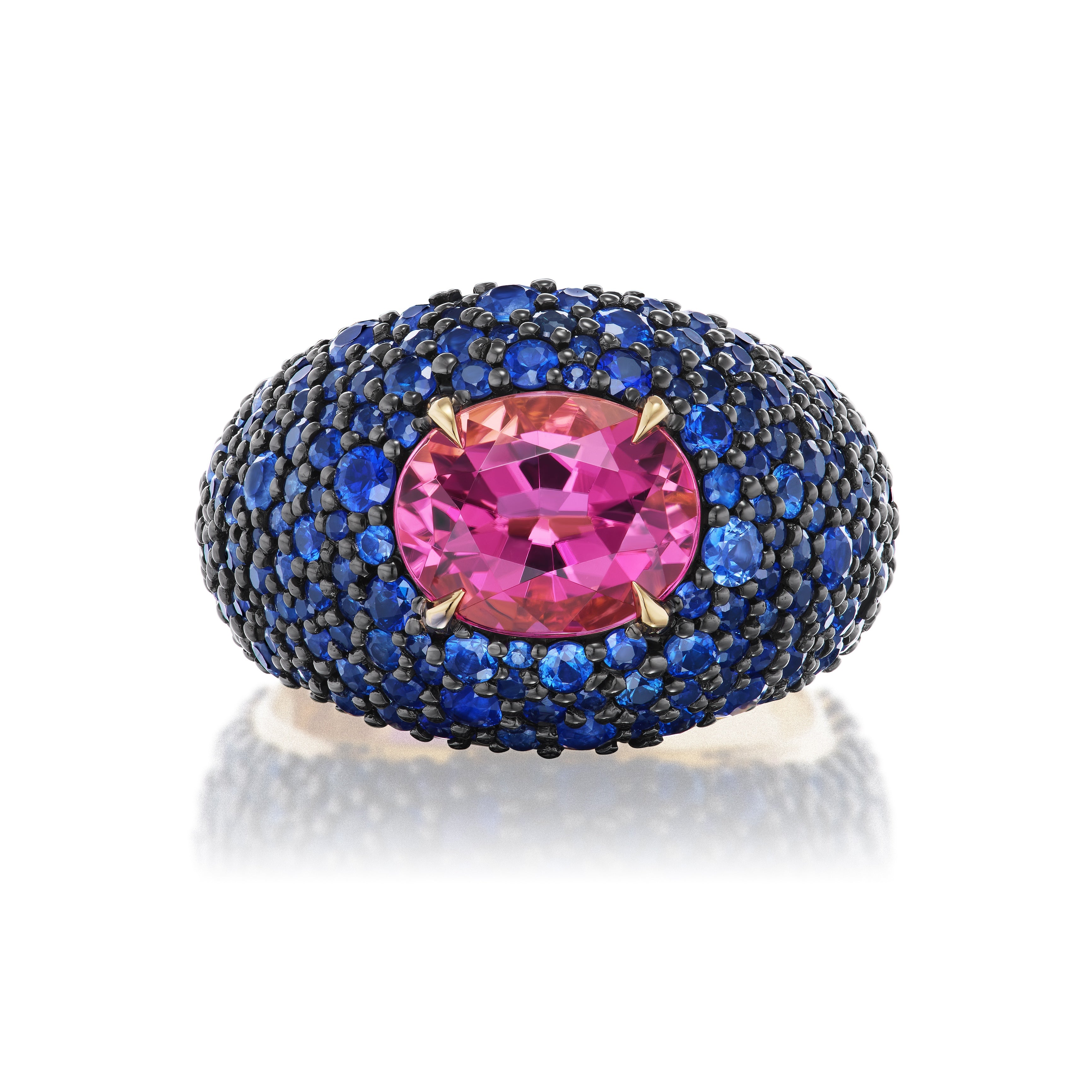 The Cobblestone Bombé Ring in Yellow Gold showcases a vibrant oval pink sapphire center, surrounded by round blue sapphires and set on a rounded yellow gold band.