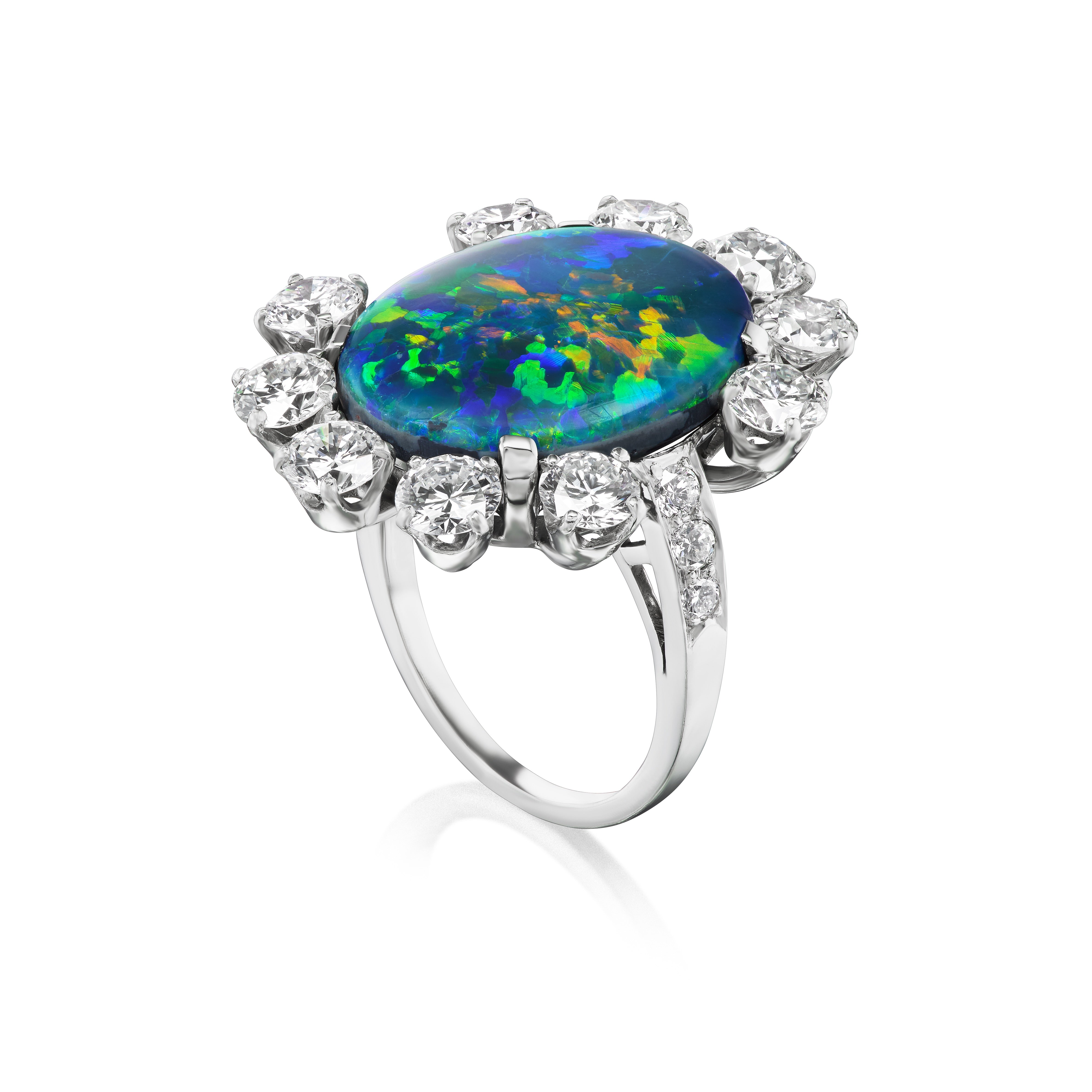 The Sunburst Oval Opal Ring with Round Brilliant Diamonds and Pavé features a large oval opal with vivid blue-green hues, accented by a halo of sparkling diamonds, all set in lustrous 18K white gold.