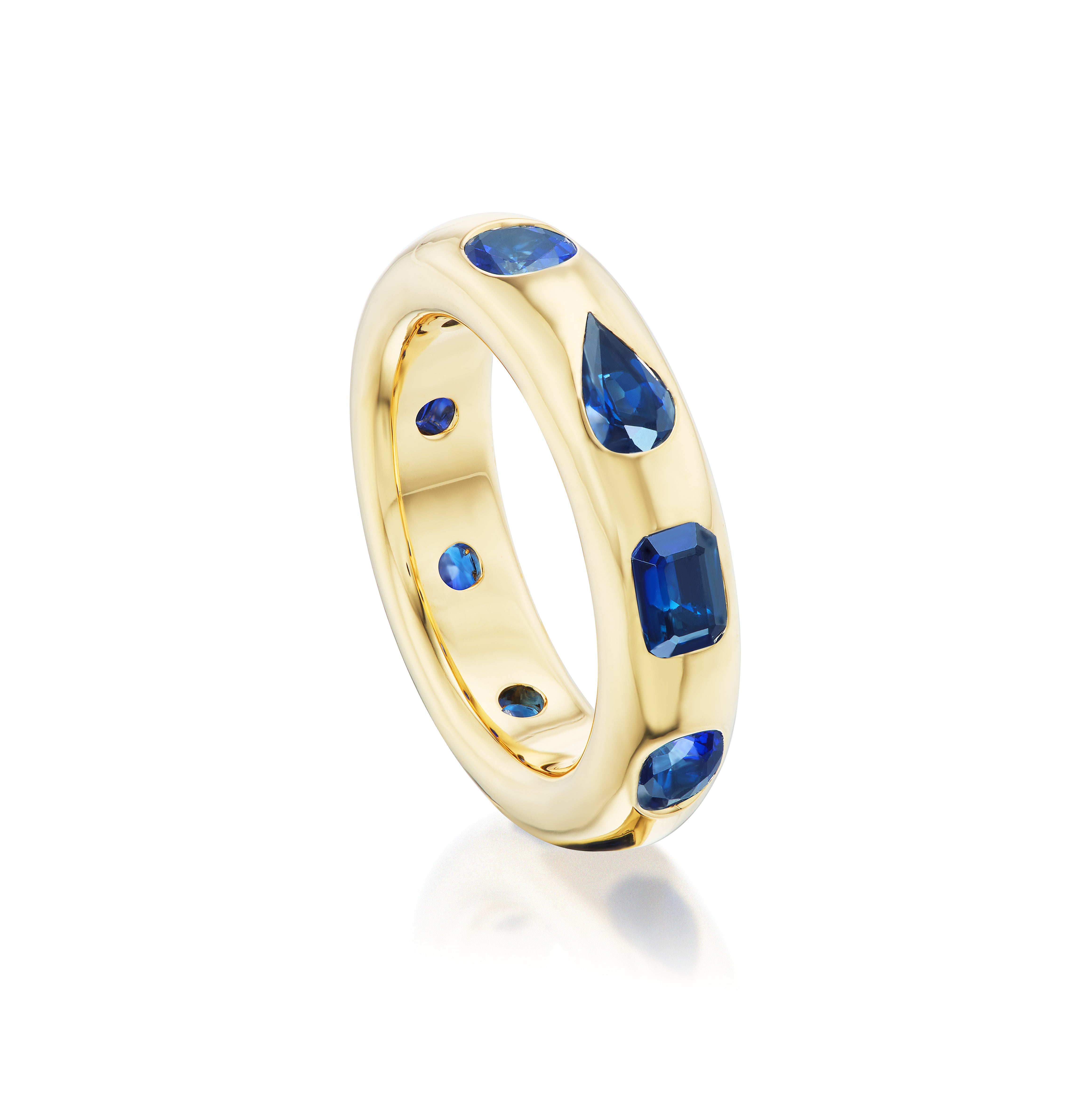 The Wedding Band in Yellow Gold features burnish-set mixed shape blue sapphires—oval, emerald cut, and teardrop—set in polished 18K gold and shown against a white background.