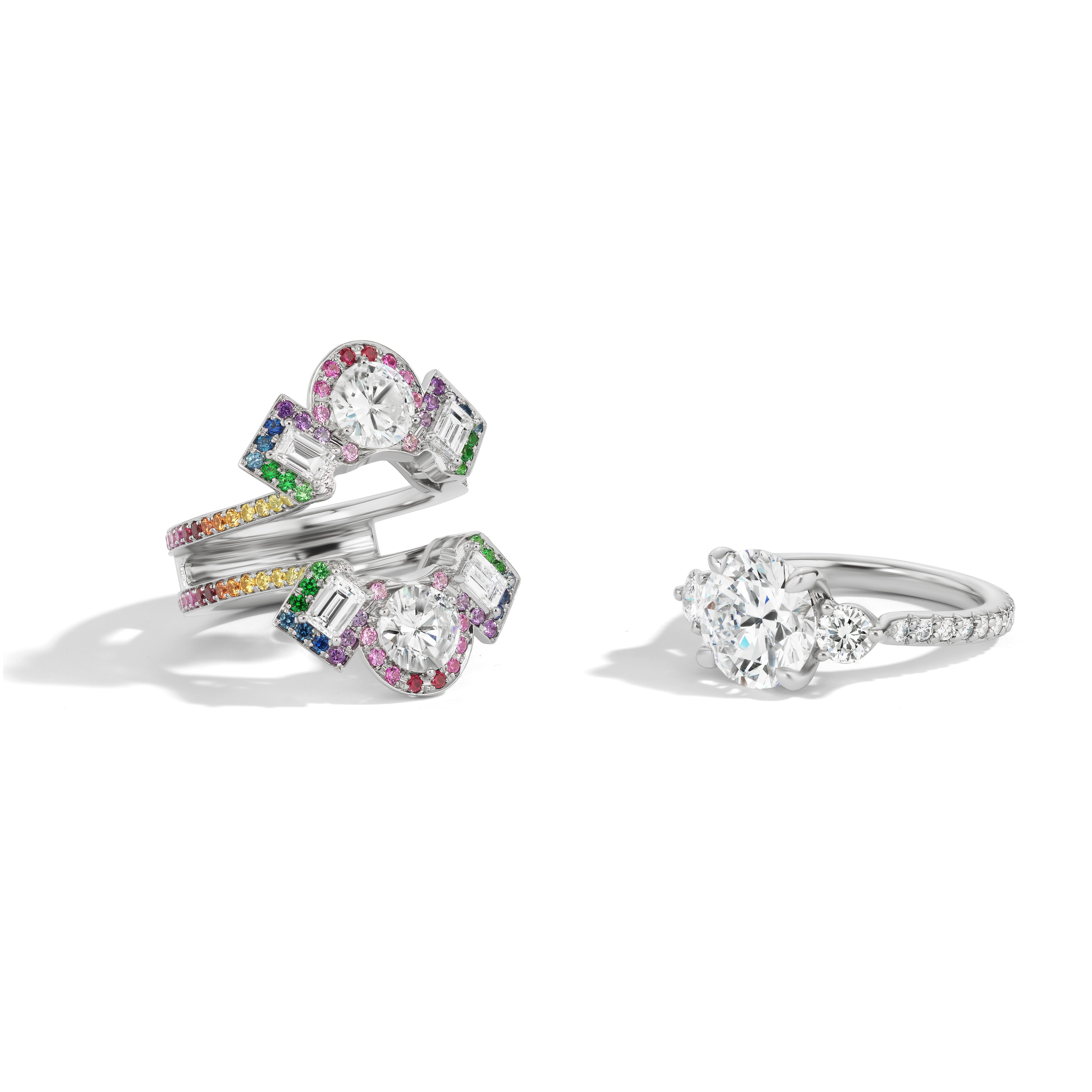 The Bespoke Cross Motif Ring Jacket features round and emerald cut diamonds with a rainbow sapphire pavé halo and band in white gold, shown on a white background.