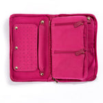 The Serpentine Travel Case in pink vegan leather is open, showing compartments, zippered pockets, and a snap-on panel for earrings or rings. Its interior features multiple sections to organize your accessories.