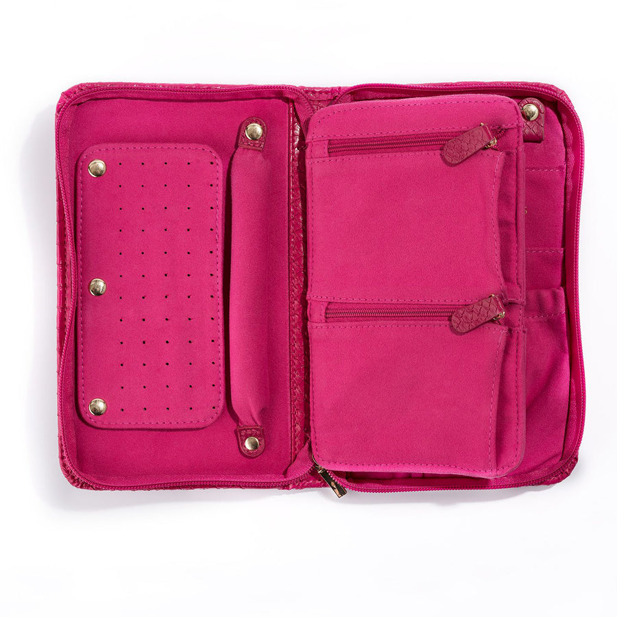 The Serpentine Travel Case in pink vegan leather is open, showing compartments, zippered pockets, and a snap-on panel for earrings or rings. Its interior features multiple sections to organize your accessories.