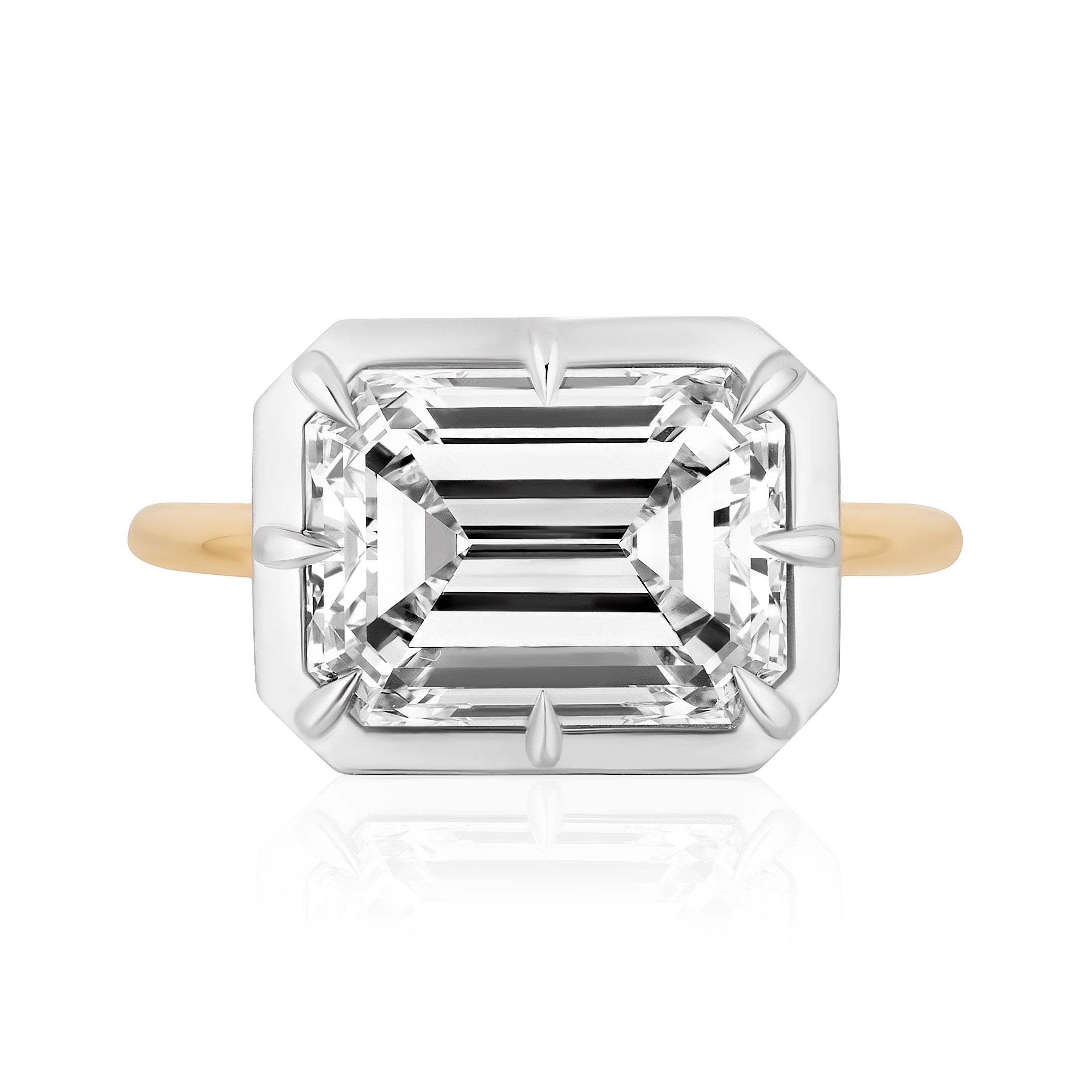 The East-West Collet Setting Emerald Cut Diamond Engagement Ring features a rectangular emerald-cut diamond in a white prong setting with a slim yellow gold band, shown against a white background.