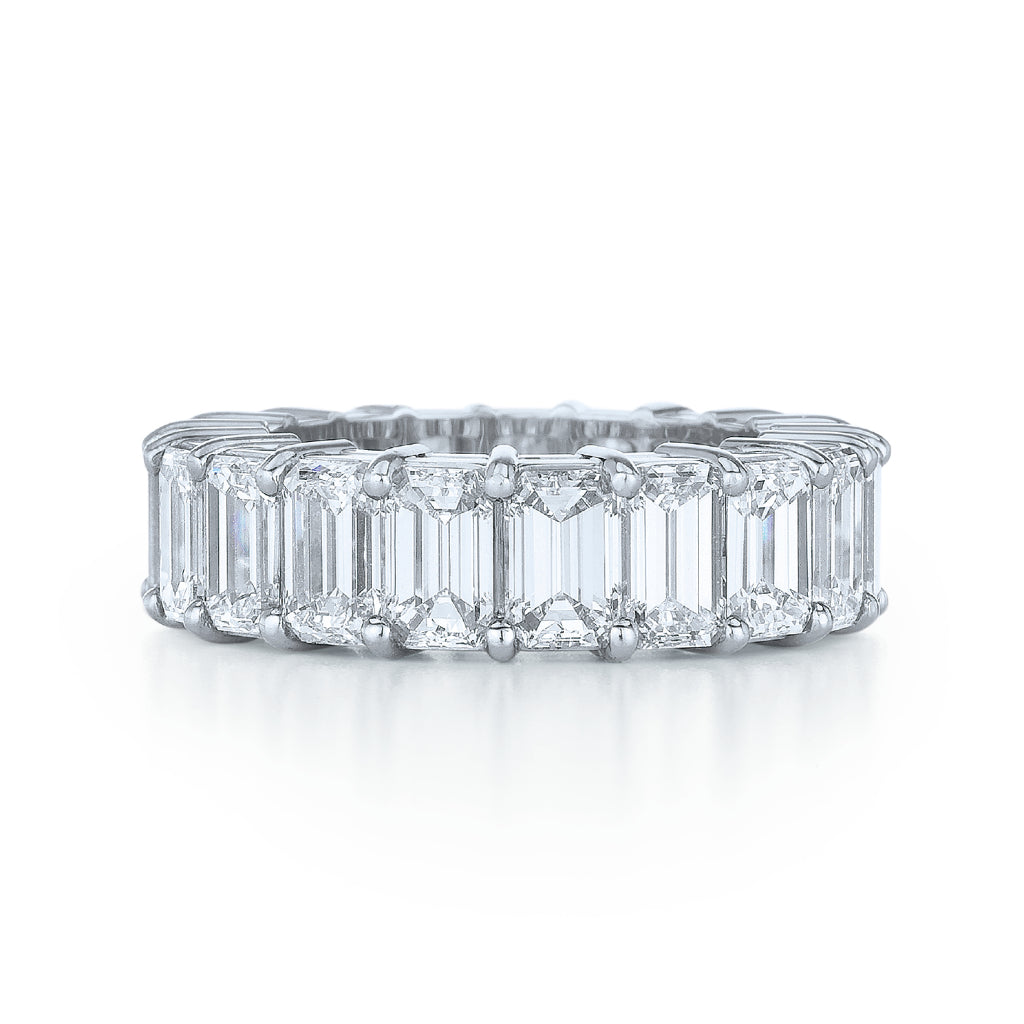The Emerald Cut Diamond Eternity Band features large emerald-cut diamonds set in platinum all around, making it a stunning bridal ring displayed against a white background.