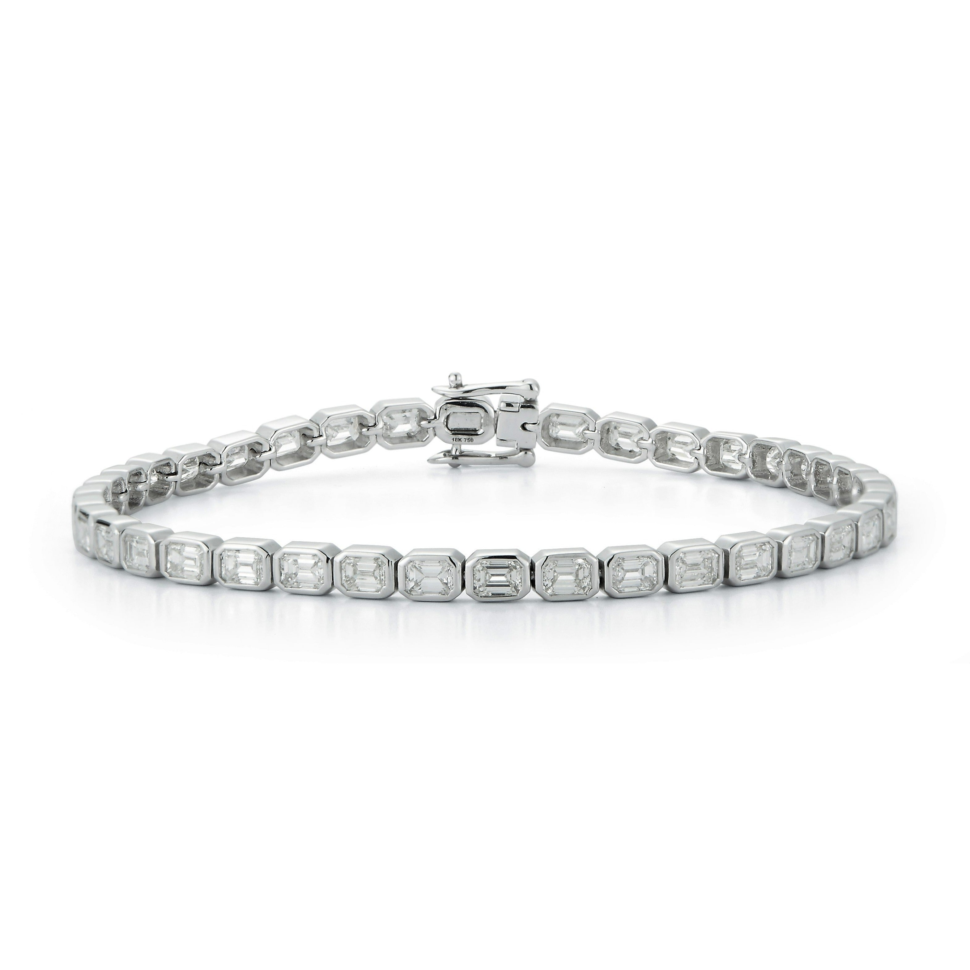The East-West Emerald Cut Bezel Bracelet features rectangular, clear emerald-cut stones set in individual silver links with a secure clasp. Displayed in a circular shape against a white background.