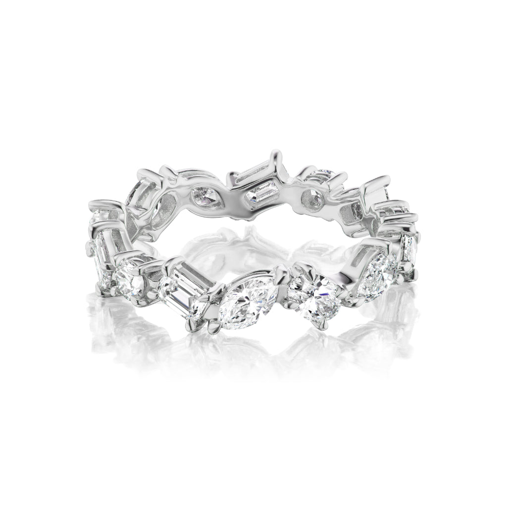 The Mixed Shape Diamond Eternity Band in 18K white gold features alternating mixed shape diamonds in a continuous design, elegantly displayed on a white reflective surface.