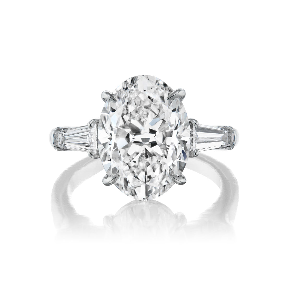 The Oval Diamond Engagement Ring with Tapered Baguette Side Stones, set on a platinum band and shown on a white background, offers an elegant and timeless choice for bridal jewelry.