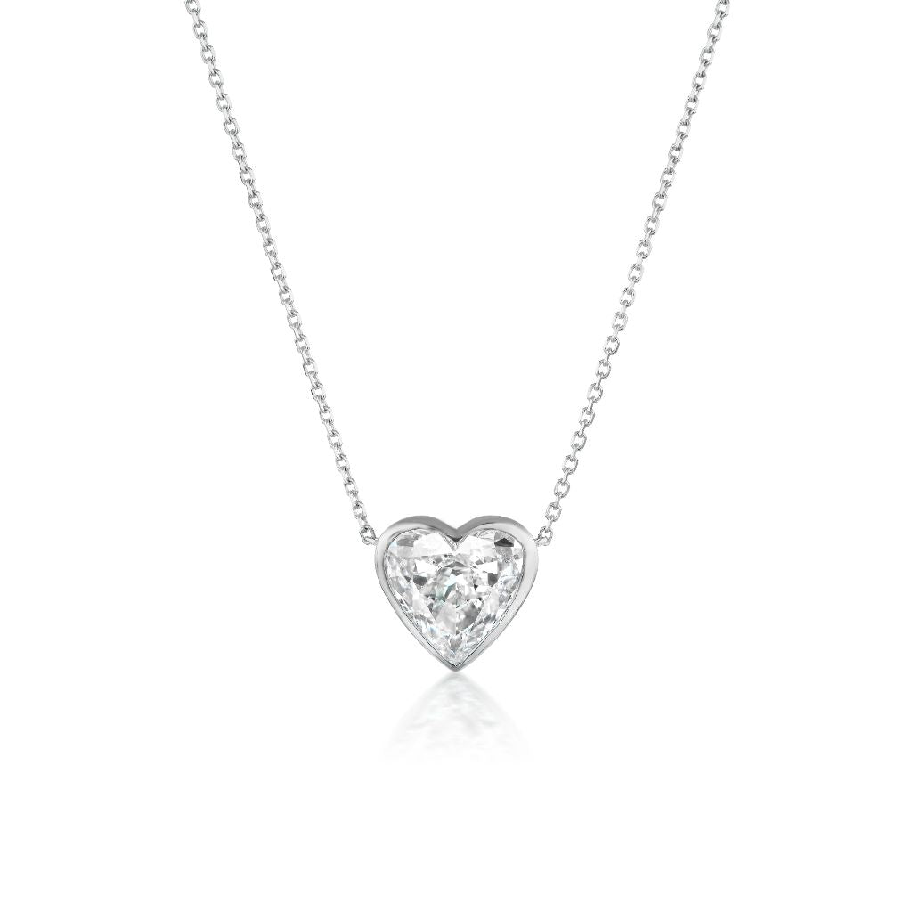 The Bezel Set Heart Diamond Solitaire Pendant in White Gold features a delicate heart-shaped diamond set in 18K white gold, elegantly displayed against a white background.