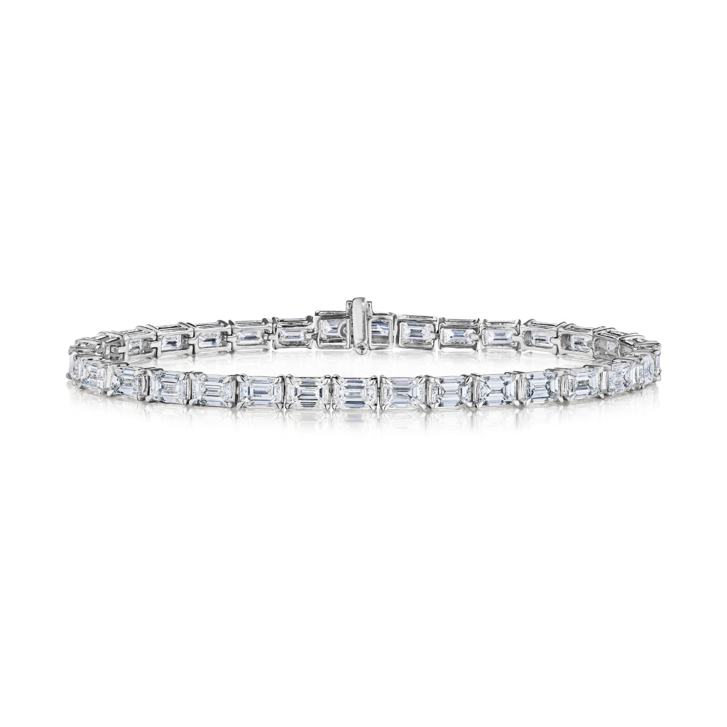 The East-West Emerald Cut Tennis Bracelet showcases emerald cut diamonds set closely in a row on a silver band, displayed against a white background.