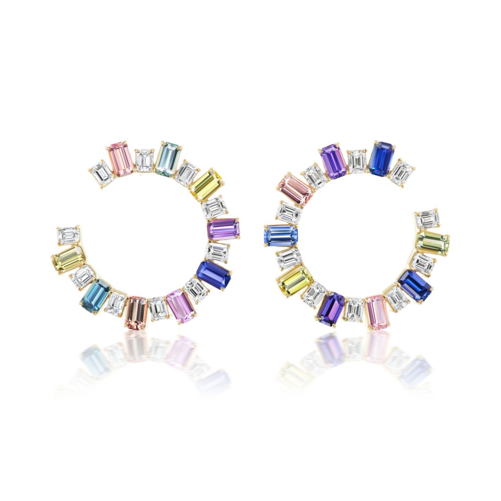 The Confetti Front-to-Back Hoops feature 18K yellow gold hoops with emerald cut diamonds and multicolor sapphires in pink, blue, purple, yellow, and clear, beautifully reflected on a white surface.