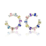 The Confetti Front-to-Back Hoops feature 18K yellow gold hoops with emerald cut diamonds and multicolor sapphires in pink, blue, purple, yellow, and clear, beautifully reflected on a white surface.