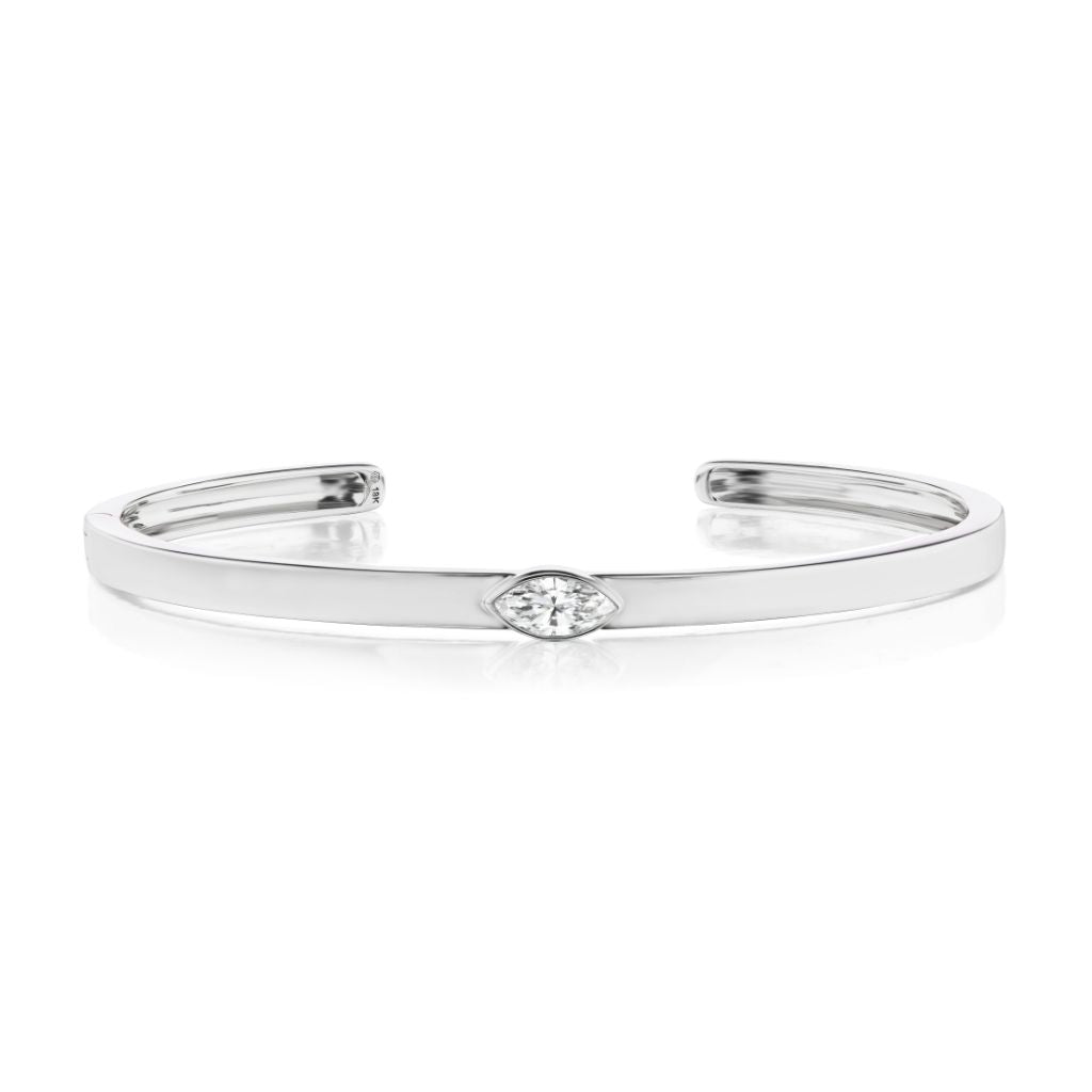 The East-West Marquise Solitaire Diamond Cuff is a sleek 18k white gold open bangle with a minimalist design, featuring a central marquise-cut diamond. Elegant and modern, this bracelet is shown on a white background.