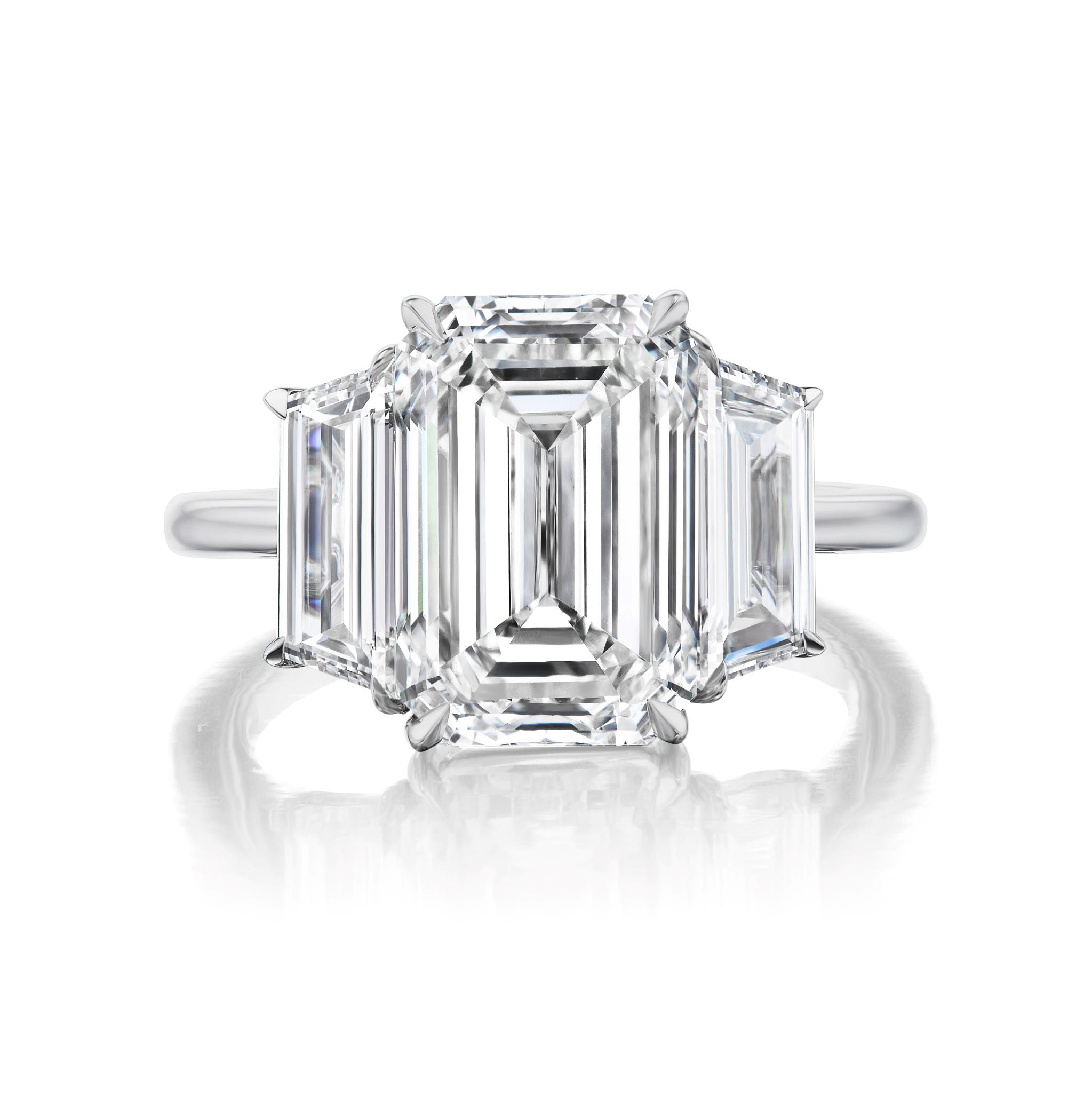 The Emerald Cut Diamond Engagement Ring with Trapezoid Side Stones showcases a central emerald-cut diamond accented by two trapezoid diamonds on each side, set in a modern, minimalist silver band.