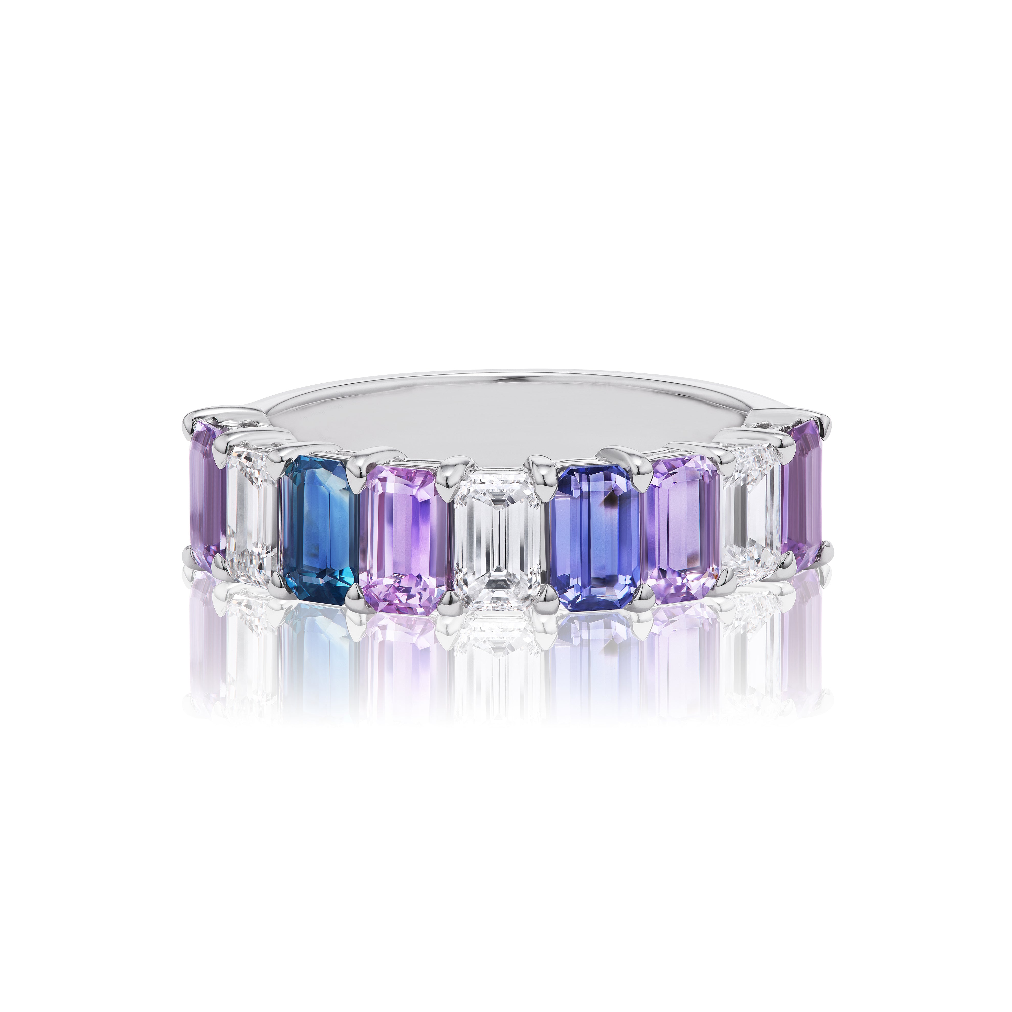 The Emerald Cut Half Eternity Band in White Gold features diamonds and multicolored sapphires in a continuous design, displayed on a reflective white surface.