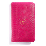 The Serpentine Travel Case is a rectangular, bright pink vegan leather wallet with a textured faux snakeskin pattern and a gold circular logo in the center, shown against a white background.