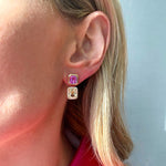 Close-up of a person with light skin and blond hair wearing Chartreuse Sapphire Pavé Ear Jackets: two stacked stud earrings, a pink square gemstone above a rectangular clear gemstone, both in 18K yellow gold.