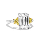 The Emerald Cut Diamond Engagement Ring features a clear center stone, fancy yellow trapezoid side stones, and white tapered baguette accents—an eye-catching choice for unique bridal rings.
