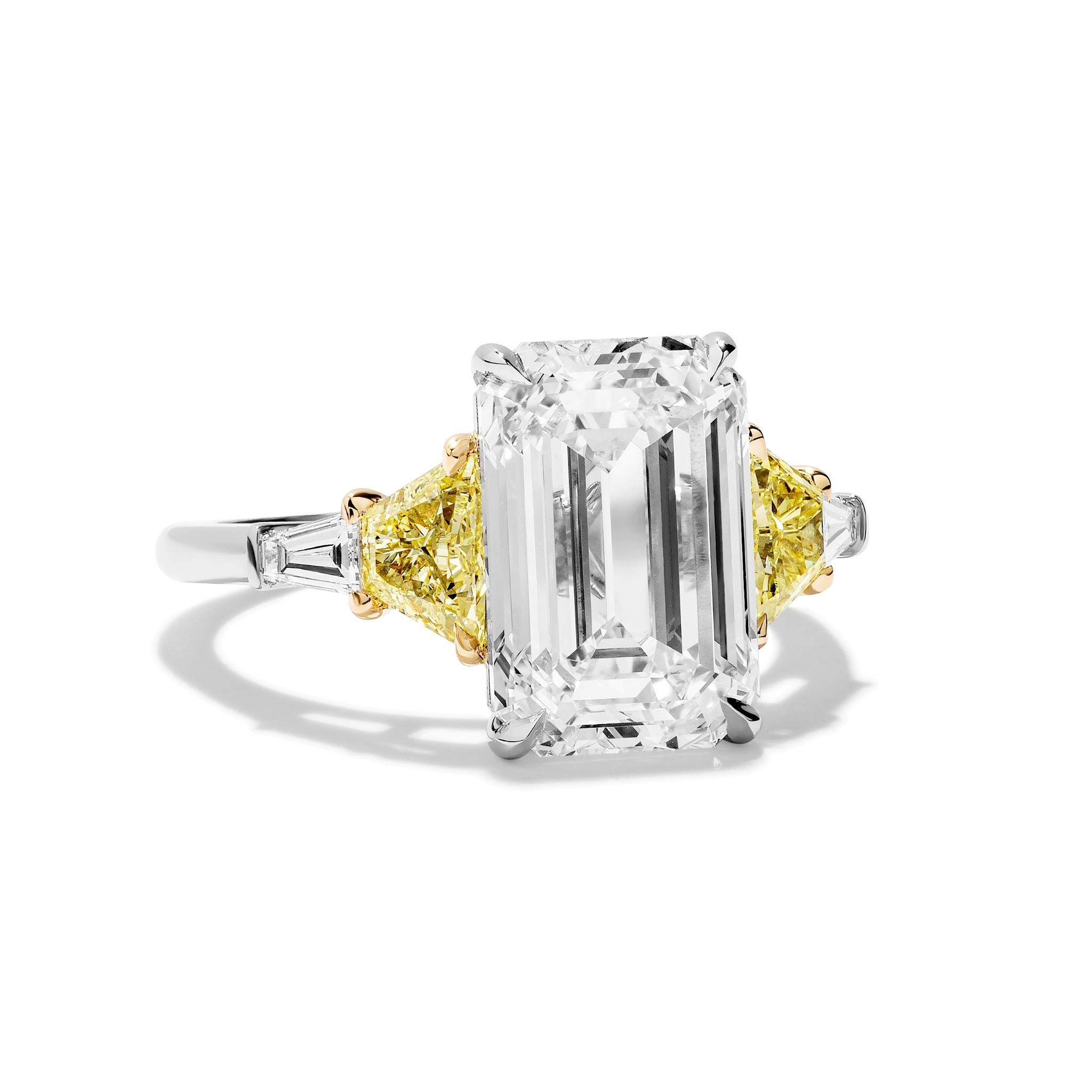 The Emerald Cut Diamond Engagement Ring features a clear center stone, fancy yellow trapezoid side stones, and white tapered baguette accents—an eye-catching choice for unique bridal rings.