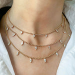 A close-up of a person’s neck wearing three layered Spike Ball Station Chain Necklaces with Pear Diamonds, styled over a white collared shirt.