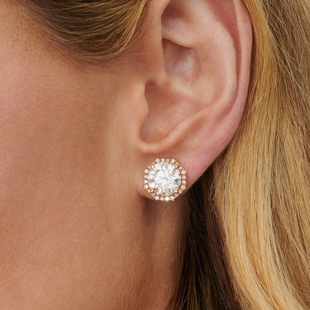 A close-up of a woman's ear wearing Pavé Octagon Ear Jackets with round brilliant diamonds in 18k gold; the large center stone is surrounded by a halo of smaller diamonds, and her blonde hair is partially visible.