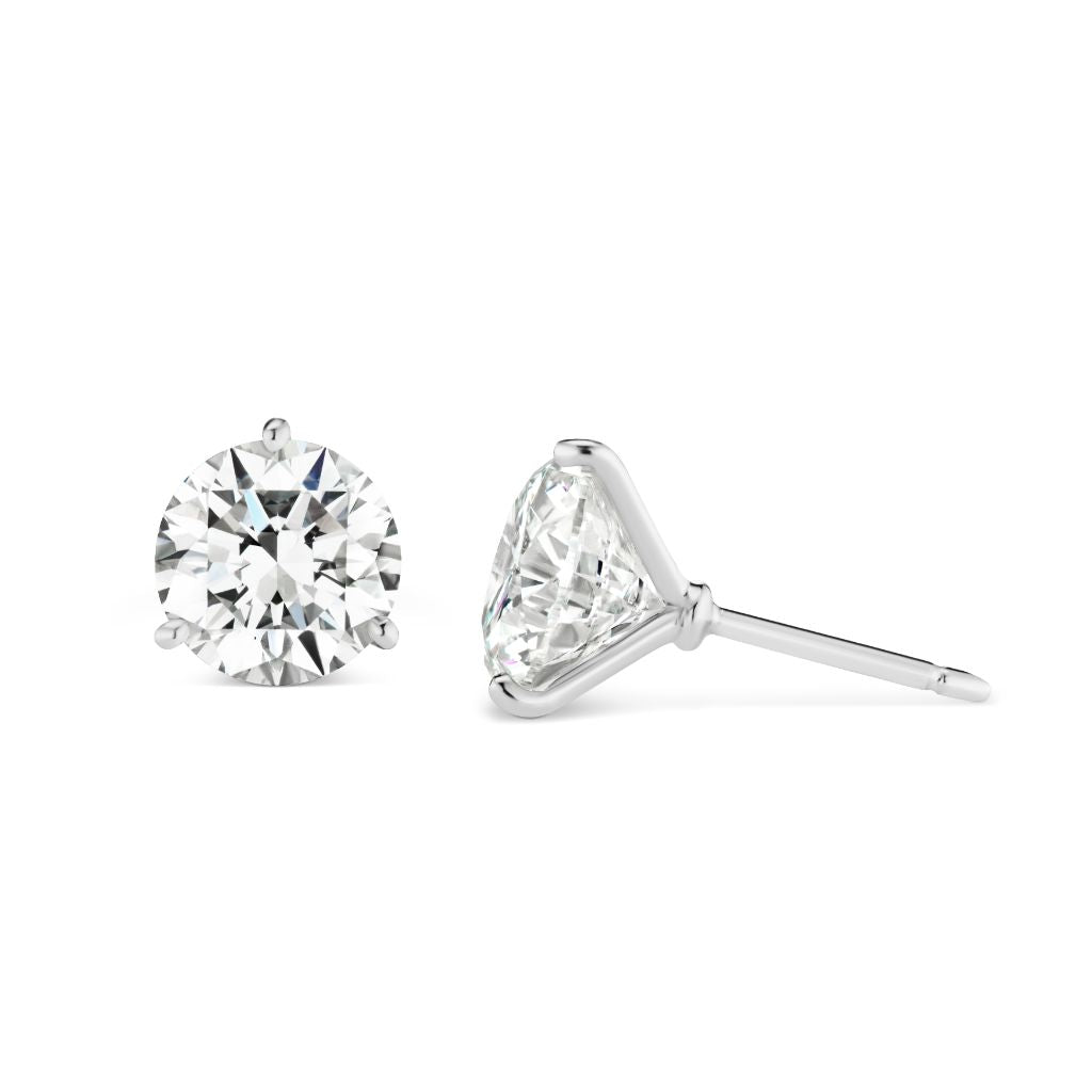 A pair of Classic Round Diamond Studs in White Gold, shown on a white background—one earring faces forward, the other is displayed from the side to highlight their elegant design.